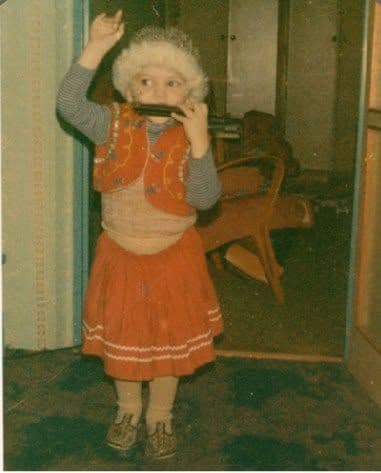 Miki as a small boy in a folk costume playing harmonica